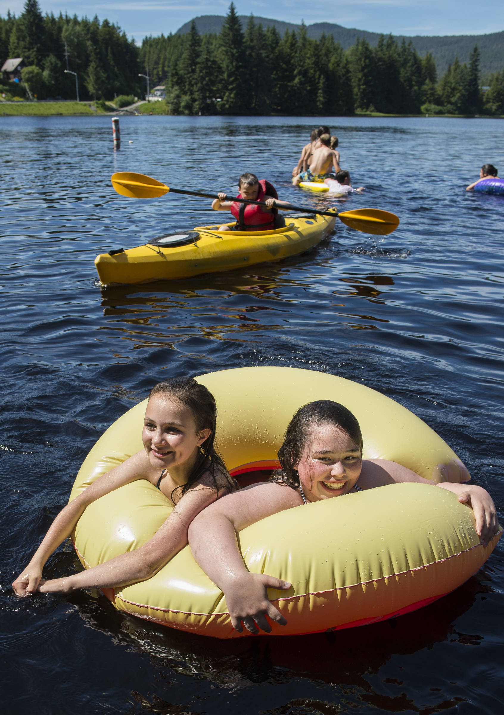 Jaden Capua-Flores, left, and Piper Robidoux, both 13, share a float as they cool off with other children at Auke Lake on Tuesday, June 19, 2018. (Michael Penn | Juneau Empire)
