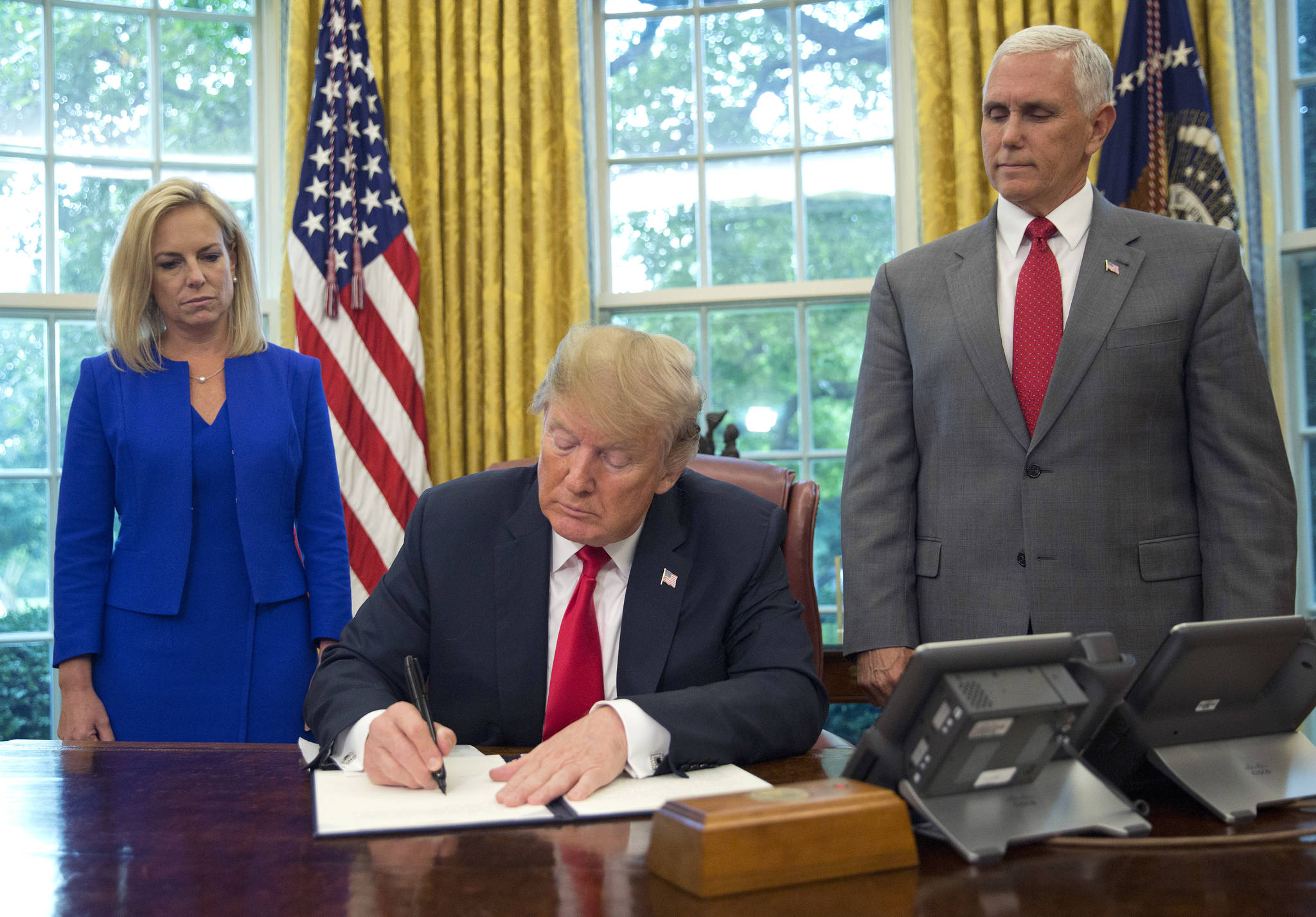 President Donald Trump signs an executive order to keep families together at the border, but says that the ‘zero-tolerance’ prosecution policy will continue, during an event in the Oval Office of the White House in Washington, Wednesday, June 20, 2018. Standing behind Trump are Homeland Security Secretary Kirstjen Nielsen, left, and Vice President Mike Pence. (Martinez Monsivais | The Associated Press)