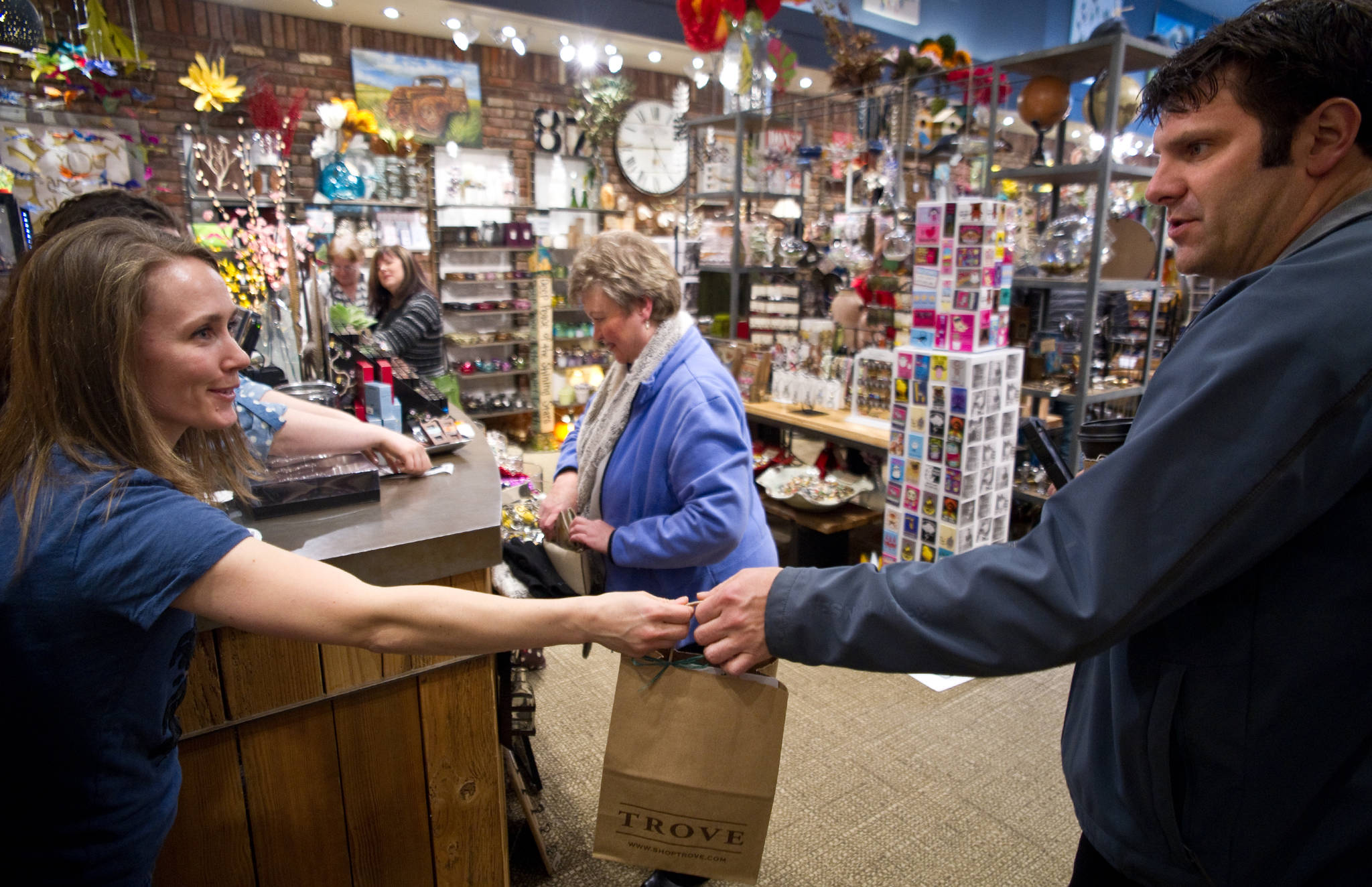 In this April 2014 photo, Trove manager Meghan Johns, left, hands Travis McCain a bag of items he bought during the cash mob orgainized by the Juneau Chamber of Commerce. (Michael Penn | Juneau Empire File)