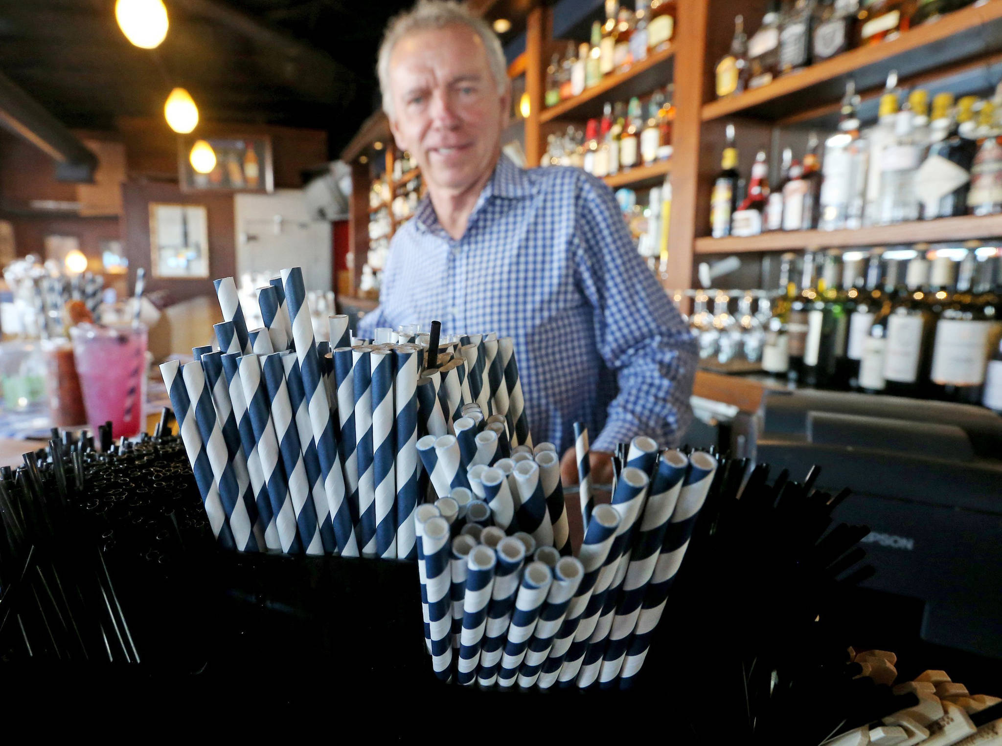 In this June 19 photo, paper straws sit in front of Duke Moscrip, owner of Duke’s, at his restaurant in Seattle. Businesses that sell food or drinks won’t be allowed to offer the plastic items under a rule that went into effect Sunday, July 1. (Greg Gilbert| The Seattle Times)