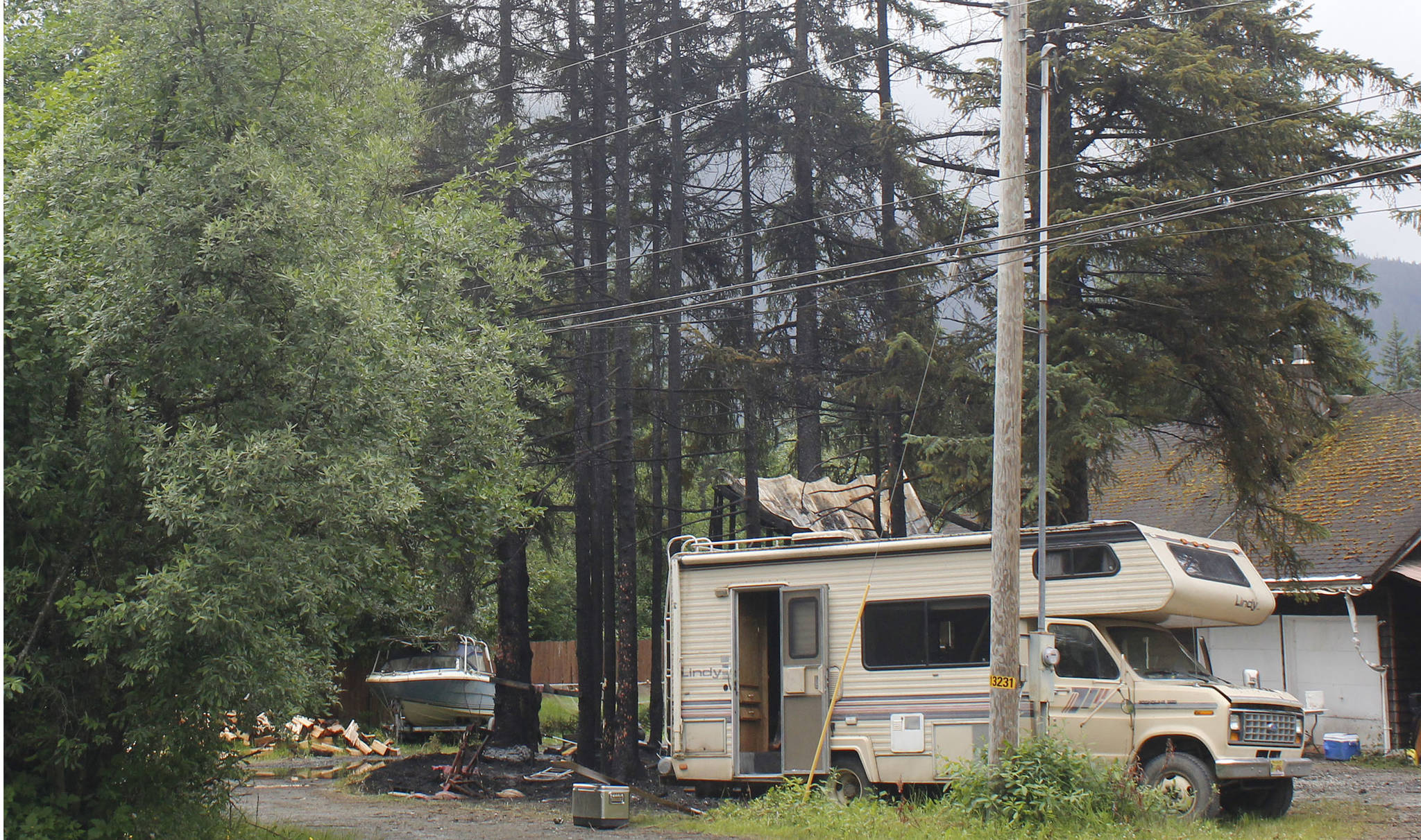 Charred trees rise above a burnt motor home and shed at a Mendenhall Valley home on July 10, 2018. An early-morning fire damaged the shed, the motor home, a fish smokehouse and a Chevy truck. (Alex McCarthy | Juneau Empire)