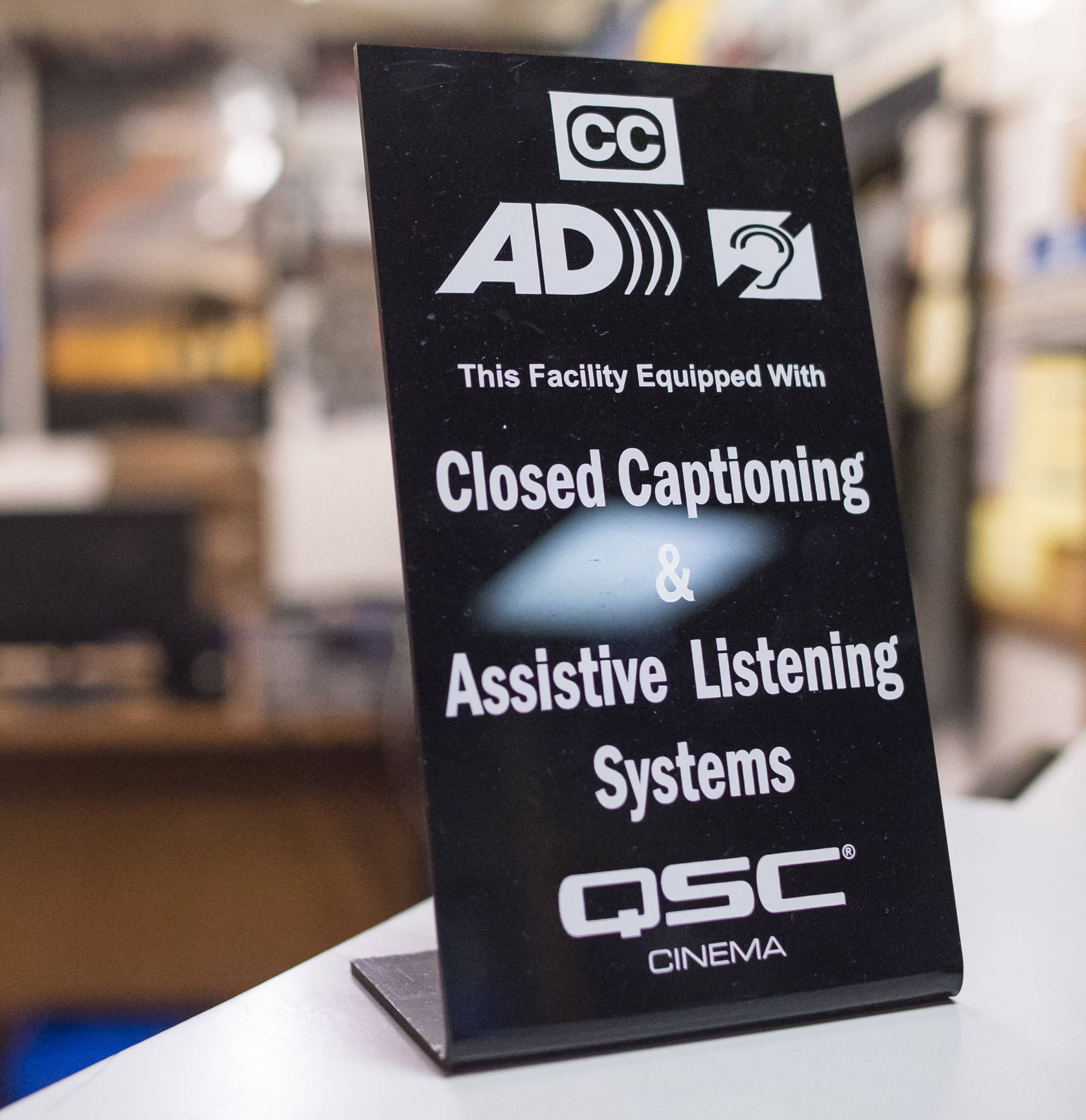 A sign announces new closed captioning and assistive listening systems at the 20th Century Theatre in downtown Juneau on Monday, July 16, 2018. The systems are available both downtown and their Glacier Cinemas in the Mendenhall Valley. (Michael Penn | Juneau Empire)