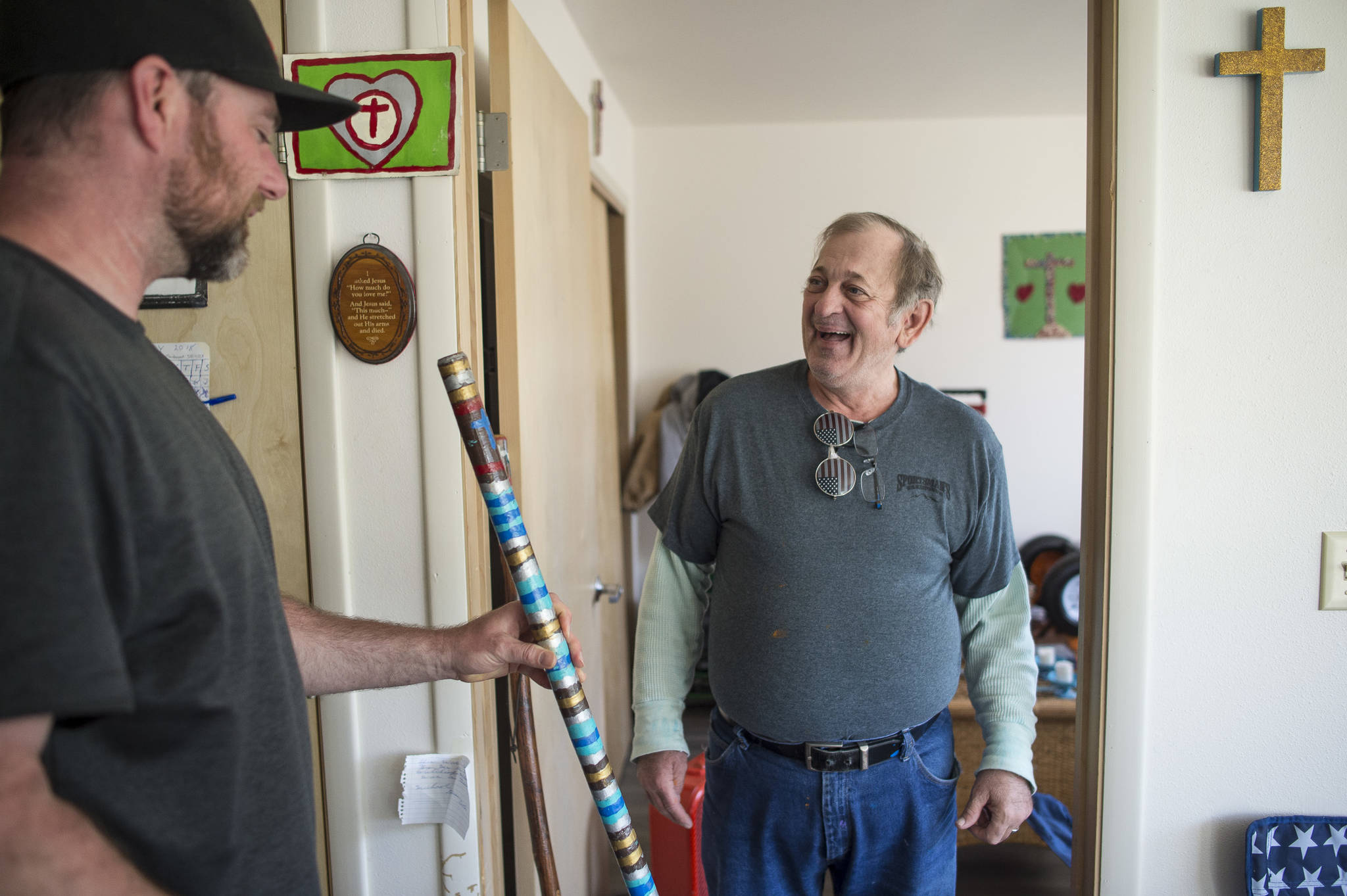 Michael Good, right, shows off his painted walking stick to Trevor Kellar, a community navigator for the St. Vincent de Paul Society, on Friday, July 20, 2018. Kellar helped Good, who has been homeless for most of his life, get a long-term apartment at the society’s Smith Hall Senior Apartments. (Michael Penn | Juneau Empire)