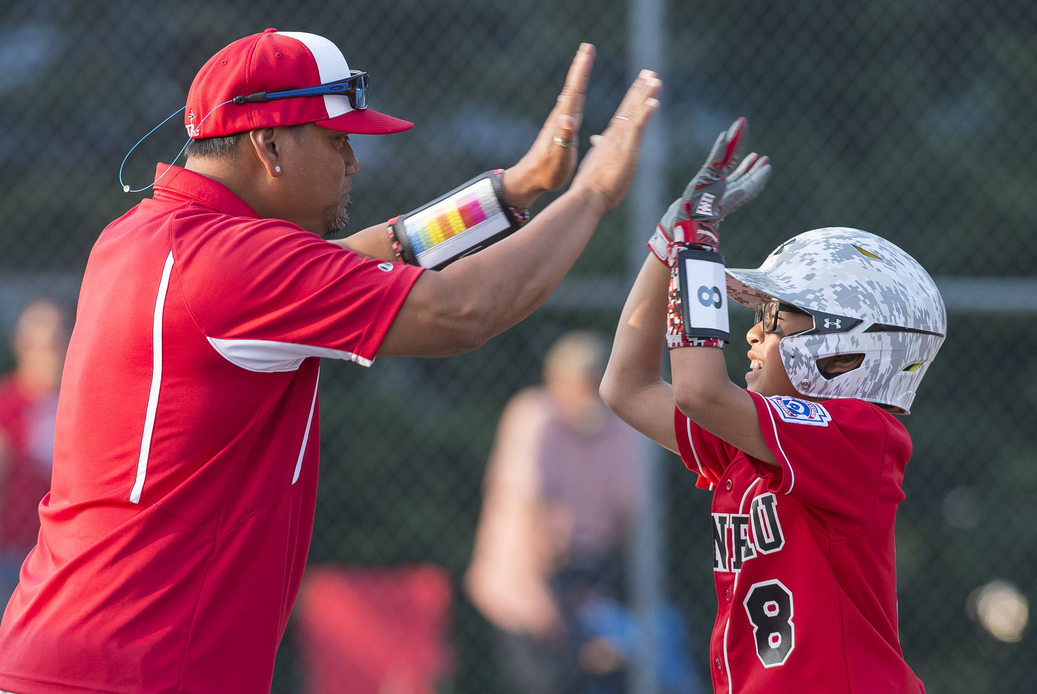 Gastineau Channel’s Erza Vidal is congratulated on a base hit by coach Randy Quinto against Ketchikan in the eighth inning of the Alaska Major Baseball District 2 Championship Game at Miller Field on Tuesday. (Michael Penn | Juneau Empire)