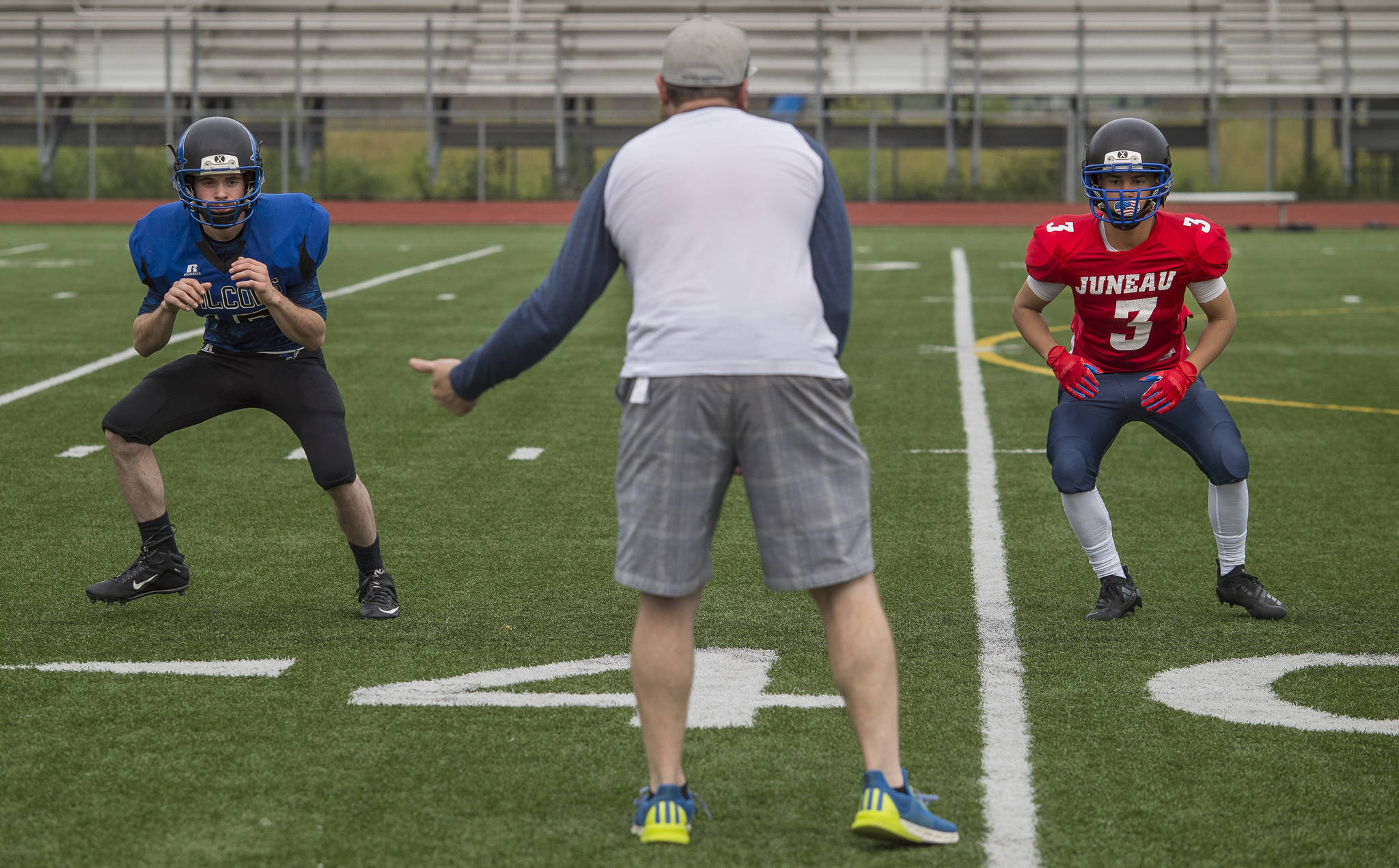 Austin Jackson, of Thunder Mountain High School, left, and Jaby Soto, of Juneau-Douglas High School, are run through a footwork drill by Todd Hansen during Juneau Football practice at Thunder Mountain High School on Thursday, July 26, 2018. (Michael Penn | Juneau Empire)