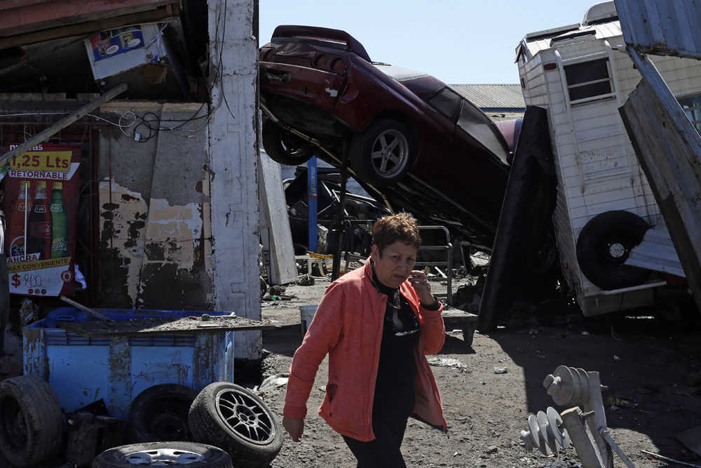 A woman walks past a car propped up between structures among the debris left behind by an earthquake-triggered tsunami Thursday in the coastal town of Coquimbo, Chile. Parts of this port city are a disaster zone after Wednesday night's 8.3-magnitude quake hit off the coast.
