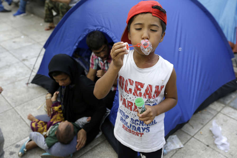 An Afghan boy blows bubbles outside his family's tent at Victoria Square, where hundreds of migrants stay temporarily before trying to continue their trip to more prosperous northern European countries, in Athens on Tuesday, Sept. 29, 2015. The International Organization for Migration says a record number of people have crossed the Mediterranean into Europe this year, now topping a half a million. Some 388,000 have entered via Greece. (AP Photo/Thanassis Stavrakis)