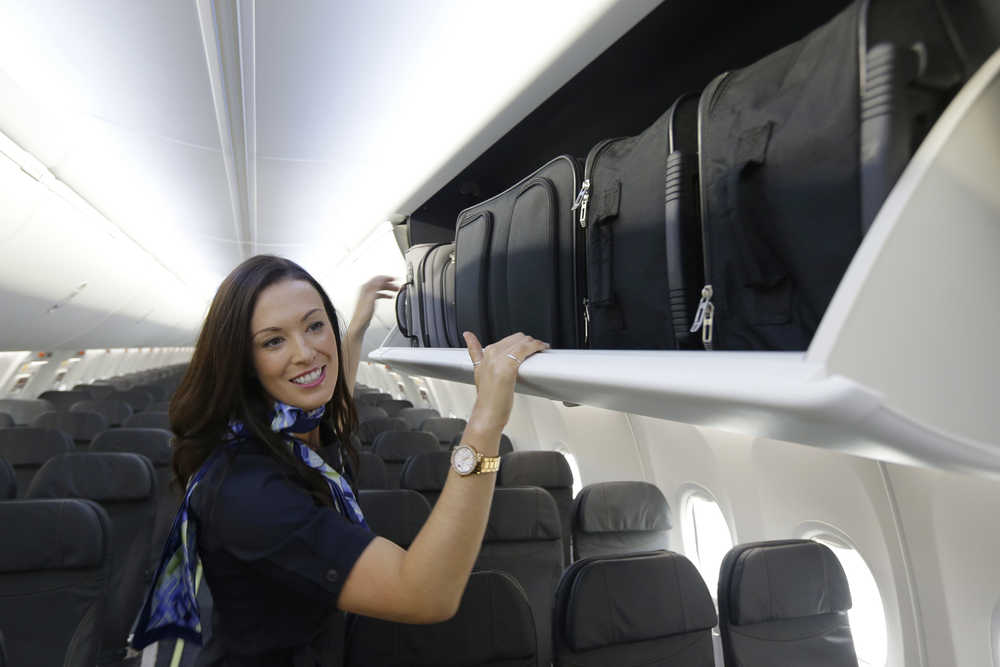 Jenn-Marie Mann, a flight attendant with Alaska Airlines, demonstrates how carry-on roller bags fit up on their sides in new larger luggage bins installed a Alaska Airlines 737-900ER airplane on Friday in Seattle. The new overhead compartments, which Boeing calls "Space Bins," can hold six standard-size bags in the same space that used to hold four. Alaska Airlines will be the first to use the new bins, both on new and retrofitted planes.