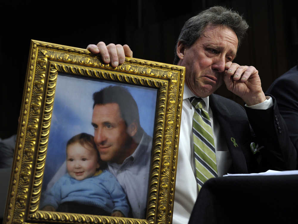 In this Feb. 27, 2013 photo, Neil Heslin, the father of Jesse, a six-year-old boy who was killed in the Sandy Hook massacre in Newtown, Connecticut, holds a picture of them together as he wipes his eye while testifying on Capitol Hill in Washington, before the Senate Judiciary Committee on the Assault Weapons Ban of 2013. The bill was defeated in the Senate.