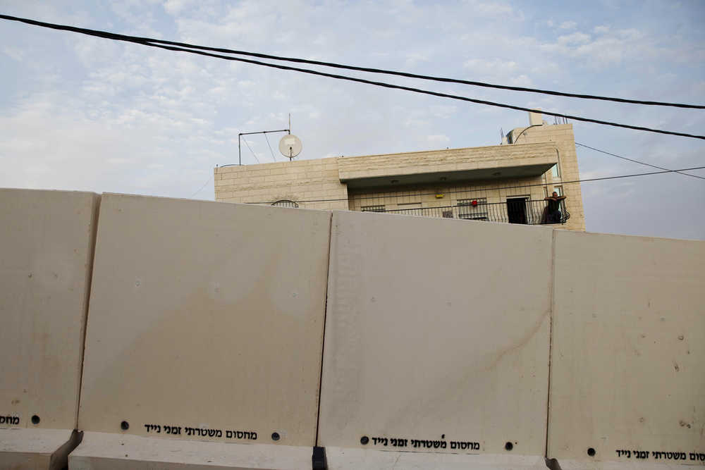 A Palestinian man stands on his balcony Sunday as he looks at concrete barrier between the Arab neighborhood of Jabal Mukaber and the Jewish area of Armon Hanatziv in east Jerusalem. I