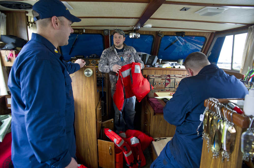 Jacob Miller, center, shows U.S. Coast Guard Petty Officer First Class Ben Stixrud, left, and Petty Officer Second Class Chris Houvener his safety gear on his 41-foot power troller at the Don Statter Memorial Boat Harbor in Auke Bay on Friday.