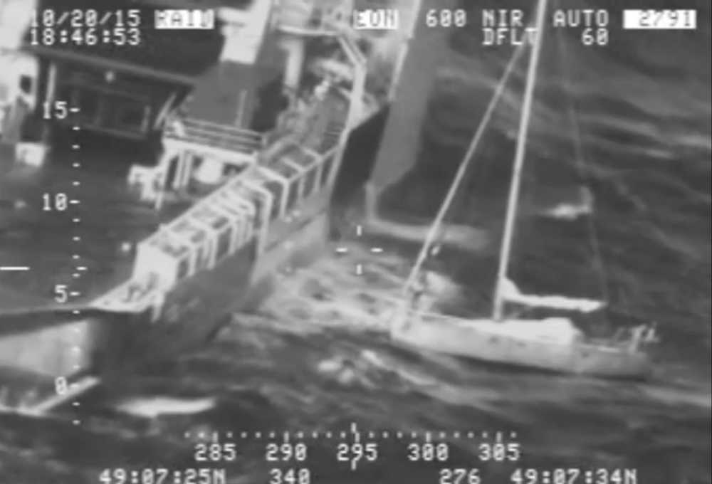 In this image from video provided by the U.S. Coast Guard, a Frenchman with his cat tucked inside his clothing, at right, stands on his saildboat before making a leap to a waiting rescue ship, left, south of Alaska on Tuesday.