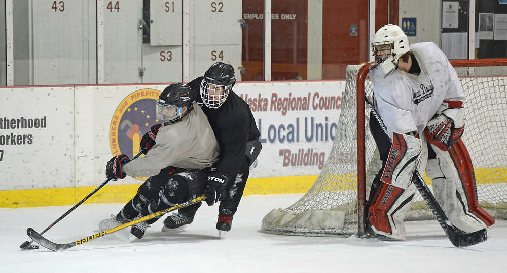 Juneau-Douglas High School senior Chase Barnum works the puck under pressure from junior Cahal Morehouse as Crimson Bears' senior goalie Nick Parise guards the corner post during Wednesday morning practice at Treadwell Arena.