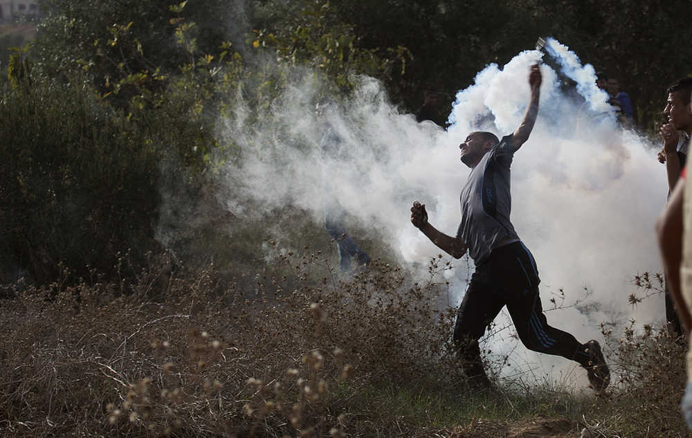 A Palestinian protester throws back a tear gas canister during clashes with Israeli soldiers by the Israeli border with Gaza on Friday, Oct. 23. Elsewhere, Muslim prayers at Jerusalem's holiest site, which has been the epicenter of weeks of unrest, ended peacefully on Friday as the first time in weeks of escalating violence, Israel allowed Muslims of all ages to enter the site to perform prayers in an apparent bid to ease tensions.