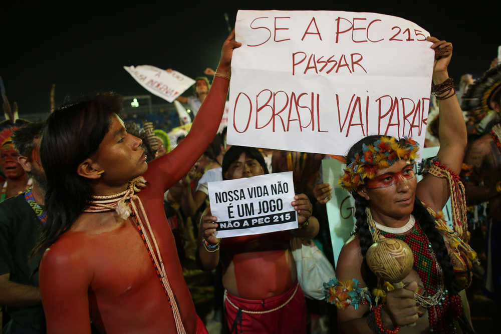 Members of Xavante indigenous from Brazil hold up signs in Portuguese that read: "If the PEC is approved, Brazil will stop," top, and "Our life is not a game" as they protest a proposed constitutional amendment that would put the demarcation of indigenous lands into the hands of the Congress Wednesday at the World Indigenous Games in Palmas, Brazil.