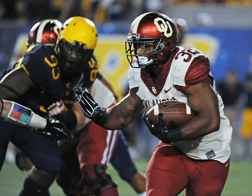 FILE - In this Sept. 20, 2014, file photo, Oklahoma's Samaje Perine (32) reaches to stiff-arm a West Virginia defender during the fourth quarter of an NCAA college football game in Morgantown, W.Va. Oklahoma's Samaje Perine rattles teeth, opens eyes and plants bad memories in would-be tacklers who are left adjusting their helmets and soothing aching muscles. Perine did all that a year ago against West Virginia, when the 243-pound tank ran for 242 yards and scored four touchdowns against the Mountaineers. On Saturday, West Virginia defenders are expecting more of the same punishment while trying to limit Perine's output when the 15th-ranked Sooners and 23rd-ranked Mountaineers meet in Norman, Oklahoma. (AP Photo/Tyler Evert, File)