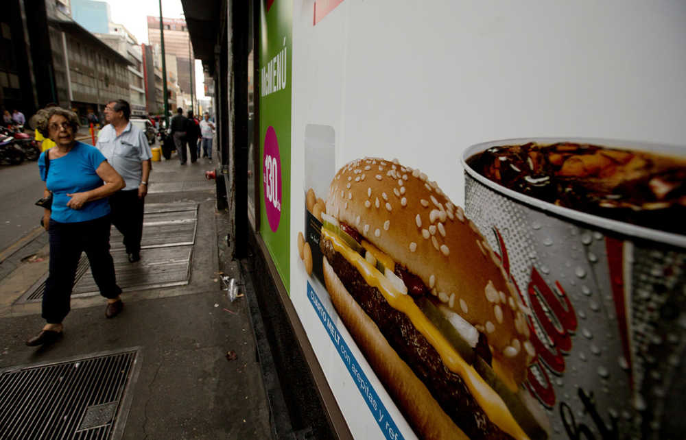 In this Jan. 6 photo, a customer glances at a McDonalds' banner menu showing a burger accompanied by arepas or corn cakes, instead of fries, in Caracas, Venezuela.