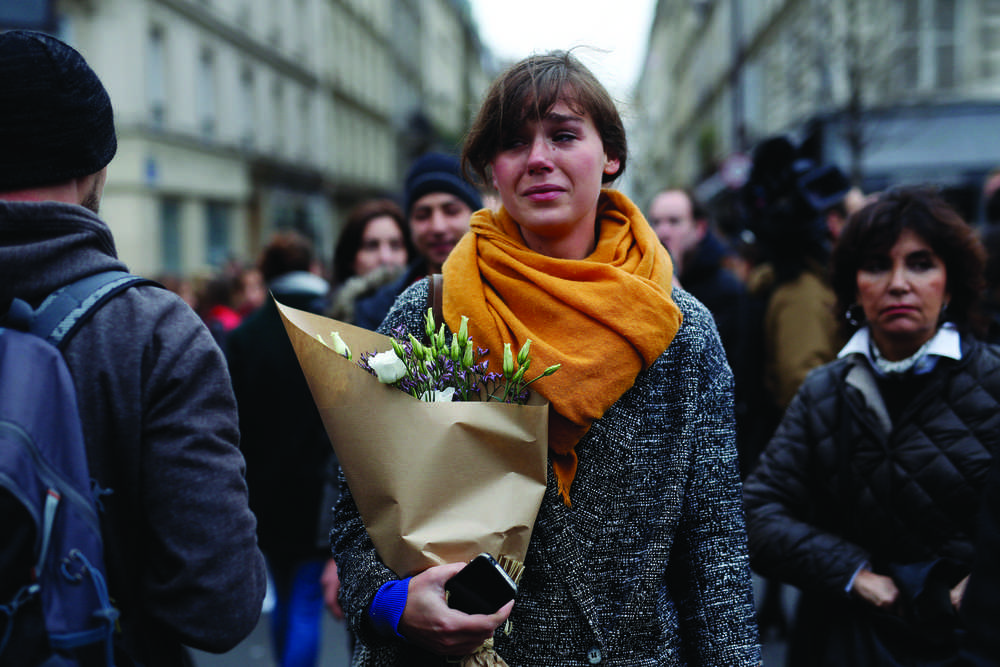 A woman carrying flowers cries in front of the Carillon cafe and the Petit Cambodge restaurant Saturday in Paris.
