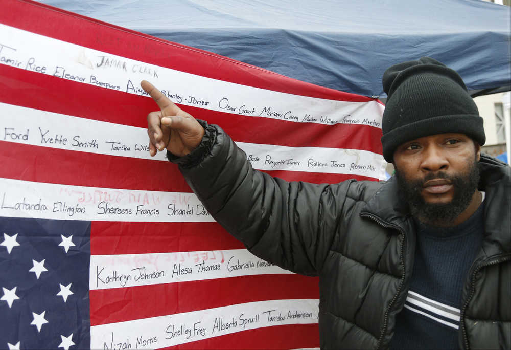 CORRECTS LAST NAME TO ROBINSON FROM CLARK - Jamine Robinson points to the name of his brother, Jamar Clark, on an upside-down flag bearing names of people killed at the hands of police outside the Minneapolis Police Department's Fourth Precinct, Tuesday, Nov. 17, 2015, in Minneapolis. Black Lives Matter demonstrators have set up an encampment at the precinct which is near the site of the Sunday shooting of Jamar Clark by a Minneapolis police officer. (AP Photo/Jim Mone)