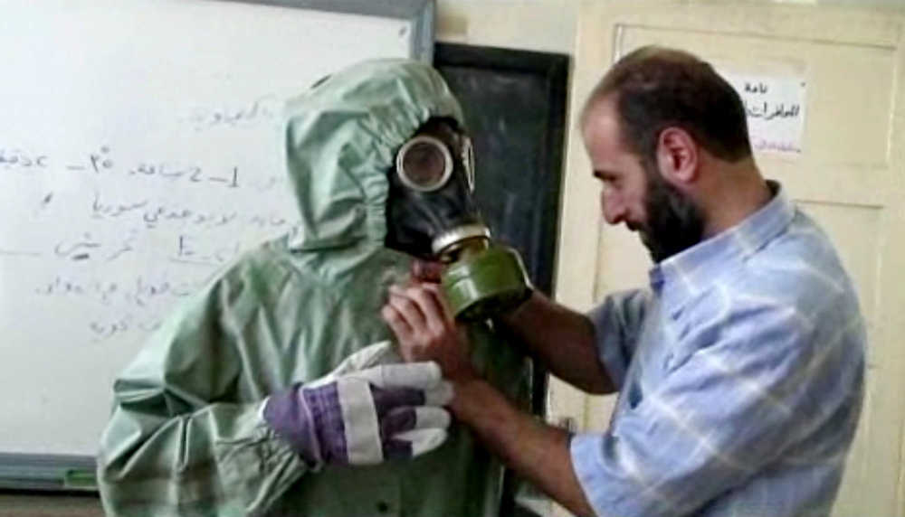 FILE - This image made from an AP video posted on Wednesday, Sept. 18, 2013 shows a volunteer adjusting a students gas mask and protective suit during a session on reacting to a chemical weapons attack, in Aleppo, Syria. The Islamic State group is aggressively pursuing development of chemical weapons, setting up a branch dedicated to research and experiments with the help of scientists from Iraq, Syria and elsewhere in the region, according to Iraqi and U.S. intelligence officials. (AP Photo via AP video, File)