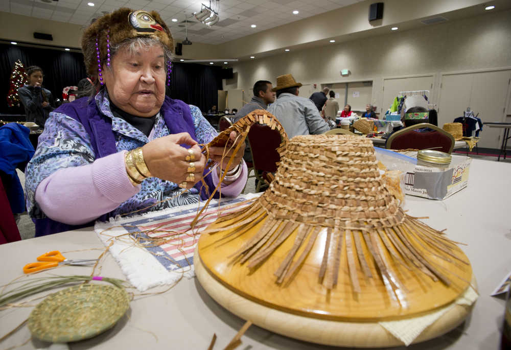 Percy Kunz works with red and yellow cedar bark to make a childs hat at the Native Artists Market in the Elizabeth Peratrovich Hall on Friday.