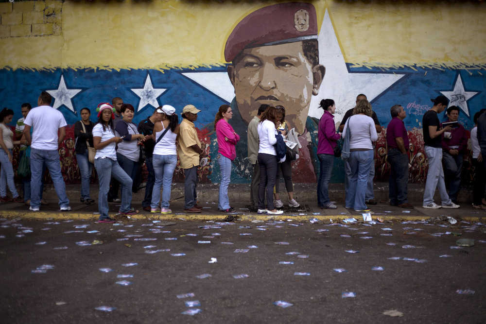 A mural of Venezuelan's late President Hugo Chavez decorates a wall outside a polling station where voters wait to enter during congressional elections in Caracas, Venezuela, Sunday.