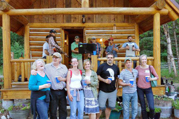 Alaskan authors, from left, Dana Stabenow, John Straley, Emily Wall, Leigh Newman, Don Rearden, Seth Kantner, and visiting keynote speaker Mary Roach stand in front of a newly completed cabin at the Alderworks Alaska Writers & Artists Retreat in Dyea during the Northwords Writers Symposium in May 2015. Not shown is Northwords faculty member Christine Byl. In the background are Skagway band Skagway band Windy Valley Boys.