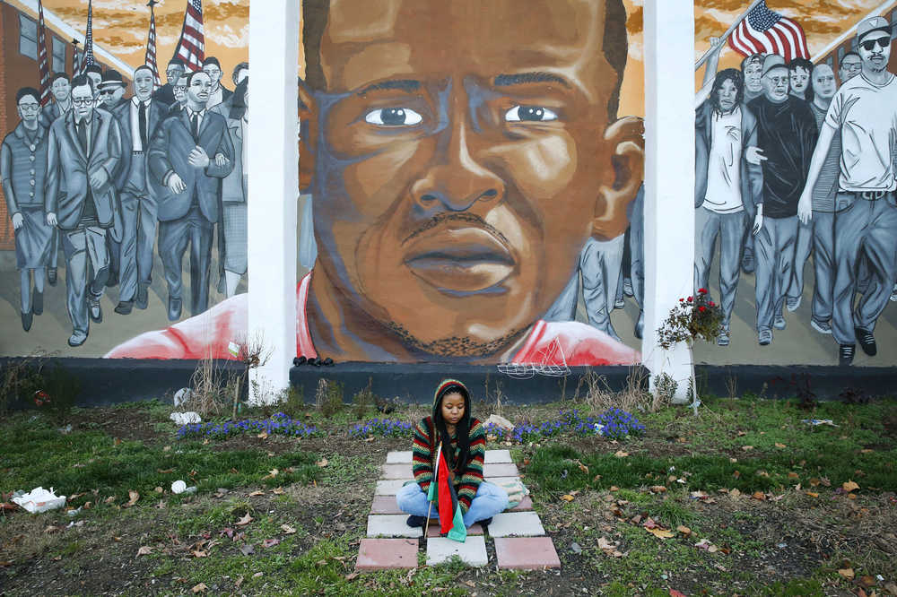 Jazmin Holloway sits below a mural depicting Freddie Gray at the intersection of his arrest, Wednesday, Dec. 16, 2015, in Baltimore. The first effort to find a police officer criminally responsible for Freddie Gray's death from a broken neck in a police van ended Wednesday with a hung jury and a mistrial. (AP Photo/Patrick Semansky)