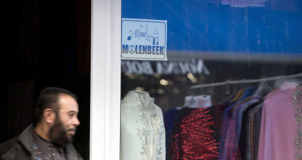 In this Nov. 18 photo, a shopkeeper walks past a sign of Molenbeek with a peace sign on it outside of his clothing shop on the main square in Molenbeek, Belgium.