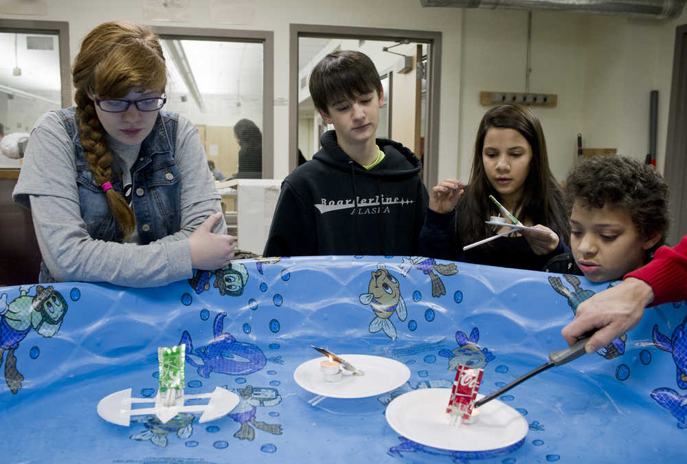 Eighth-graders Aurora Ward, left, Henry Waxenfelter, Marjorie Vonda and Chance Stovall, right, watch as their steam-powered "pop pop" boats made out of aluminum cans are put to the test in teacher Alan Degener's technology class at Floyd Dryden Middle School on Friday.