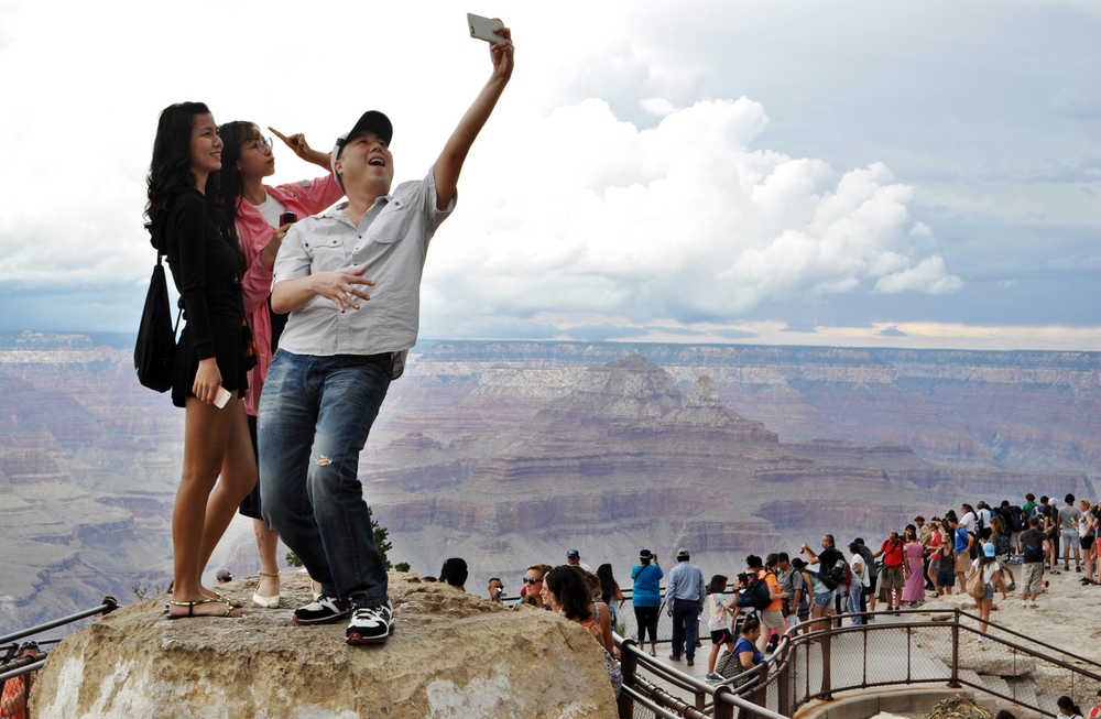 In this Aug. 2 photo, tourists Joseph Lin, Ning Chao, center, and Linda Wang, left, pose for a selfie along the south rim at Grand Canyon National Park, Arizona.