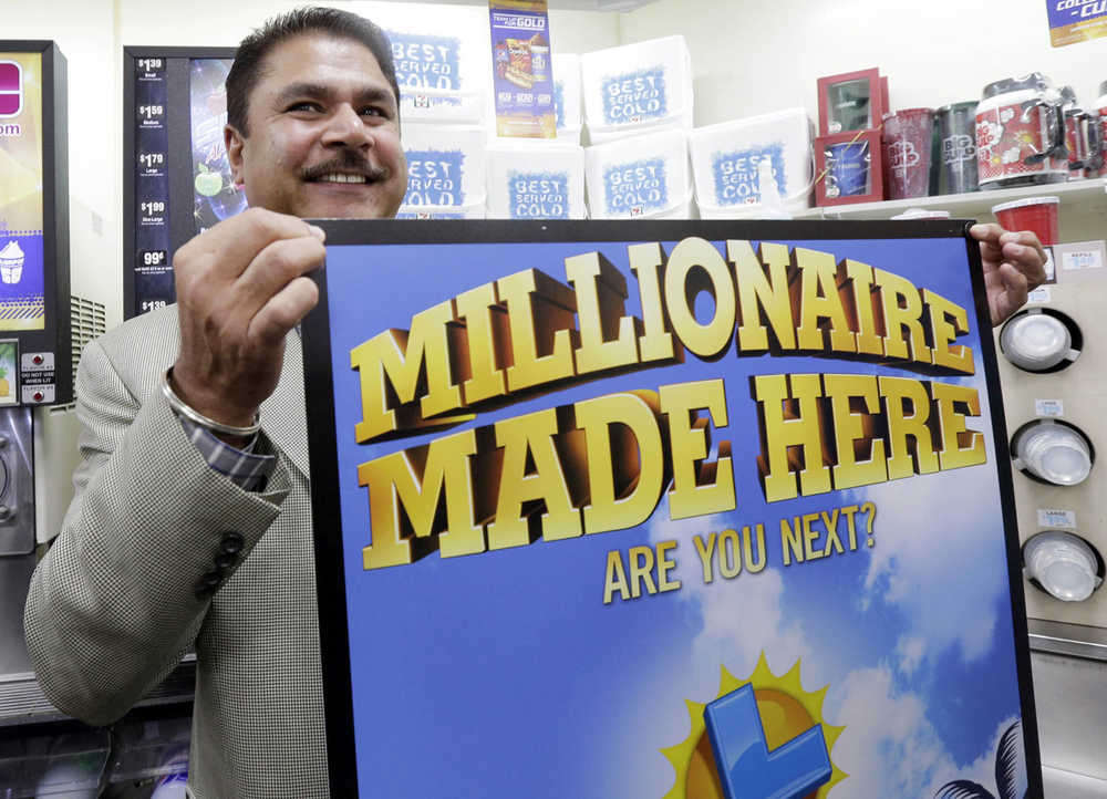 Balbir Atwal, the owner of a 7-Eleven store that sold a winning Powerball lottery ticket, holds up a Millionaire Made Here sign at his store in Chino Hills, California on Thursday.