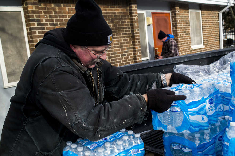 Maintenance technicians Mike Young, front left, and Chris Sprague deliver cases of water to residents on Tuesday, Jan. 19, 2016 at River Park Apartments in Flint, Mich. After weeks without water being distributed, the residents are finally getting bottled water delivered to their doorsteps for the first time by the Flint Hoursing Commision. (Jake May/The Flint Journal-MLive.com via AP)