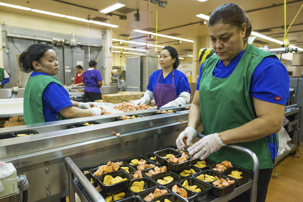 In this photo taken Jan. 13, from left, Jackie Garcia, Chieu Montgomery, and Carmen Sanchez prepare meals of whole grain chicken nuggets and maple sweet potato cubes at the Anchorage School District nutrition center in Anchorage.