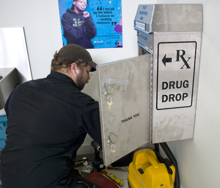 Sergei Morosan of the CBJ buidling maintanance department installs a new prescription drug drop box in the lobby of the Juneau Police Department on Tuesday, July 7, 2015.