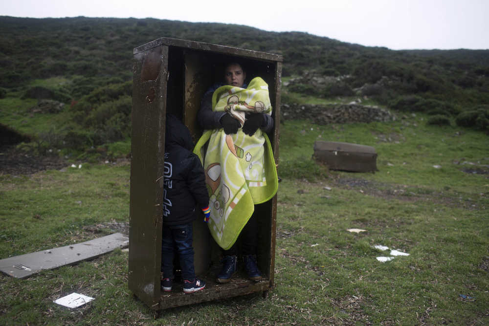 A Syrian woman with her children takes a shelter in a iron box during a rainfall, after they arrived from Turkey to the Greek deserted island of Pasas near Chios on Wednesday, Jan. 20, 2016. Thousands of migrants and refugees continue to reach Greece's shores despite the winter weather. (AP Photo/Petros Giannakouris)