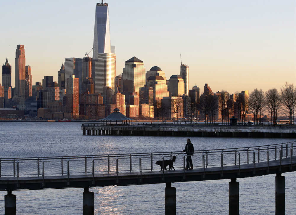 A man walks his dog along the waterfront at sunset Wednesday in Hoboken, New Jersey, where the Lower Manhattan skyline serves as a backdrop.