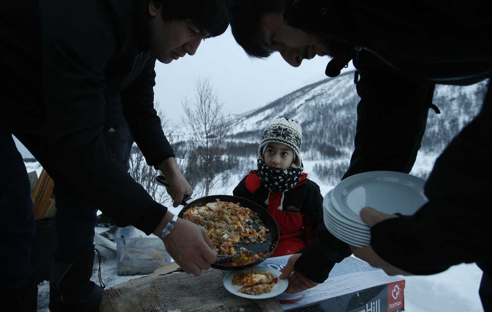 Afghan asylum seeker Roheek Yausofi waits his turn for food cooked on an open fire, with fish caught the day before by his father, on the island of Seiland, northern Norway, Feb. 2.