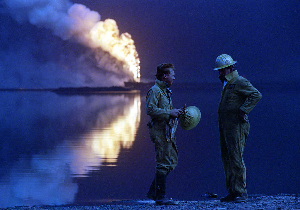 FILE -- In this July 30, 1991 file photo, oil well firemen from a U.S. company discuss the day's work while a wellhead burns out of control across a lake of crude oil in the Ahmadi oil field, Kuwait.  Twenty five years after the first U.S. Marines swept across the border into Kuwait in the 1991 Gulf War, American forces find themselves battling the extremist Islamic State group, born out of al-Qaida, in the splintered territories of Iraq and Syria. Oil prices, which sparked Saddam's invasion of Kuwait, have dropped to under $30 a barrel from more than $100 in just a year and a half. (AP Photo/John Gapps III, File)