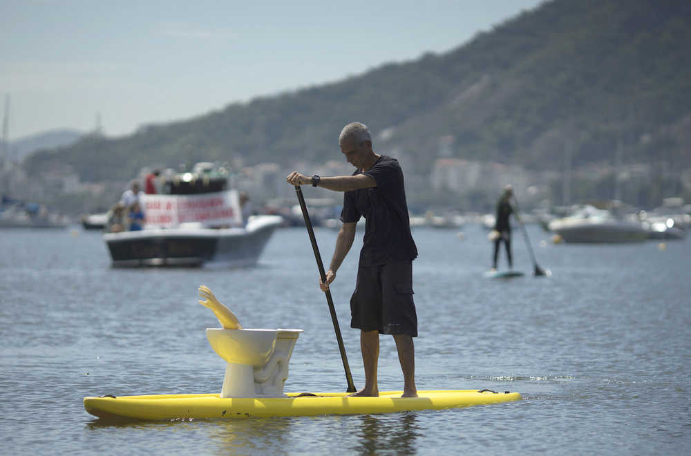 A man paddles his board, with a toilet and a plastic arm on top of it, during a demonstration against the pollution of the Guanabara bay, in Rio de Janeiro, Brazil, Saturday, Feb. 27, 2016. Activists alleging that decades of neglect and authorities' repeated failure to make good on cleanup promises have effectively killed one of Rio de Janeiro's most iconic waterways where Olympic sailing competitions are to be held. (AP Photo/Leo Correa)