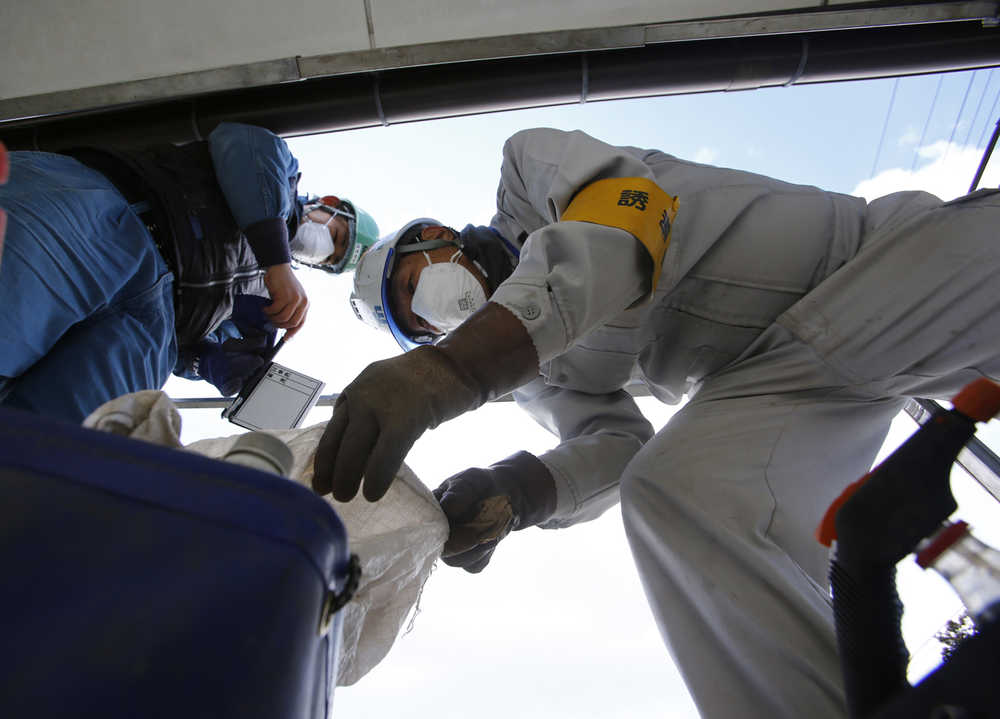 In this Feb. 24 photo, workers wearing masks collect radioactive waste at a private house's garden in Minamisoma, Fukushima Prefecture, northeastern Japan.