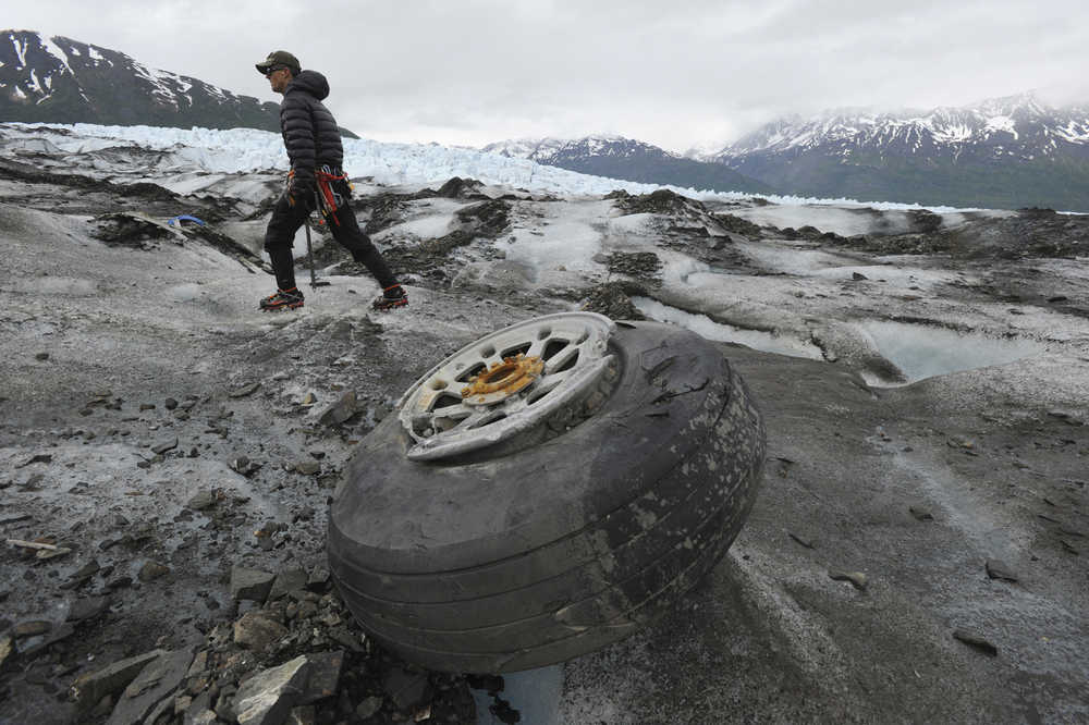 In this June 10, 2015 photo, U.S. Marines Capt. David Gooch, with the Defense POW/MIA Accounting Agency, walks past an aircraft wheel assembly resting on the ice surface of Colony Glacier.