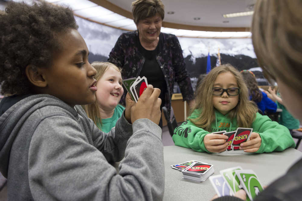 IMAGE DISTRIBUTED FOR MATTEL, UNO - Former Mayor and current Assembly member Mary Becker watches as Juneau Community Charter School students Clinton McQueen, 11, left, Brynna Morgan, 8, center, and Lamar Blatnick, 9, play a game of UNO in the Assembly Chambers in Juneau, Alaska, on Friday, April 1, 2016. As part of an April Fools' promotion, the city of Juneau and Mattel announced a renaming of Juneau to UNO. (Michael Penn/AP Images for Mattel, UNO)