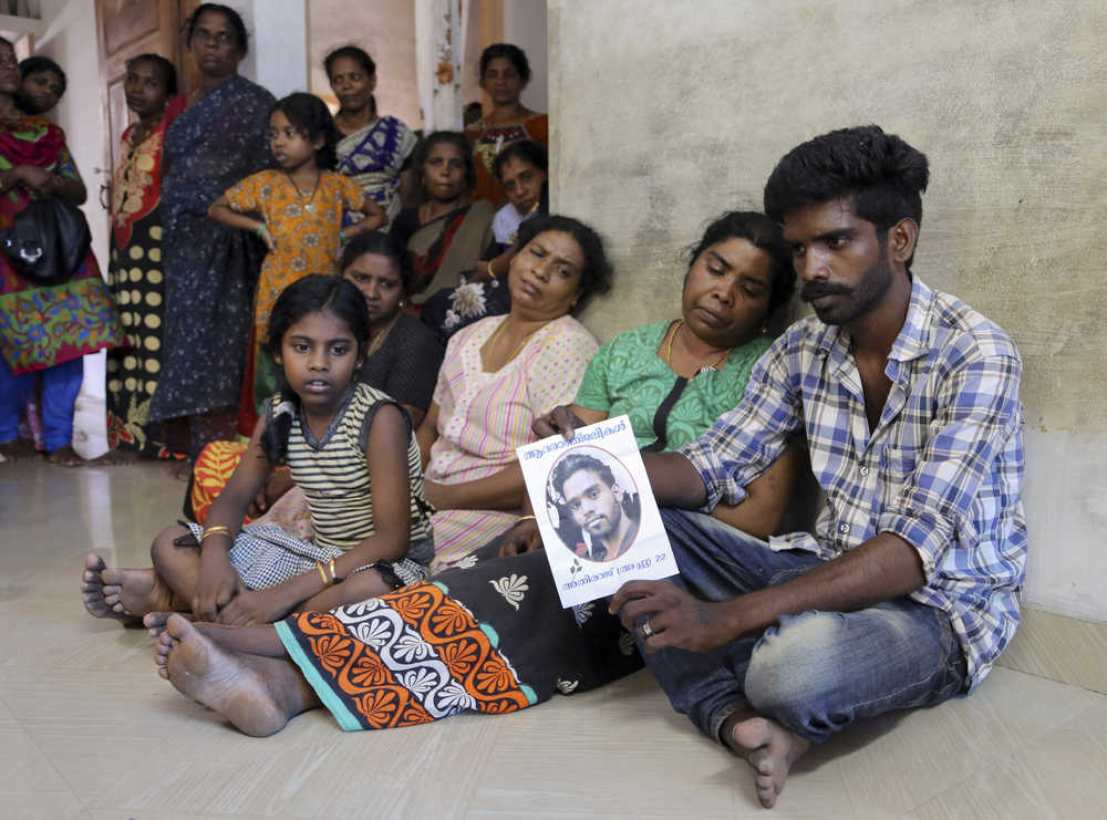 Arun Suraj, 24, right, sits next to her mother Symala, second right, and other relatives as he displays a poster which has a photograph of his brother Athiraj, 22, who died after a massive fire broke out Sunday during a fireworks display at the Puttingal temple complex in Paravoor village, Kollam district, southern Kerala state, India, Monday, April 11, 2016. Medical teams on Monday tended to hundreds of people injured in a massive fire that killed more than a hundred, while authorities searched for those responsible for illegally putting on the fireworks display that caused the weekend blaze. (AP Photo/Aijaz Rahi)