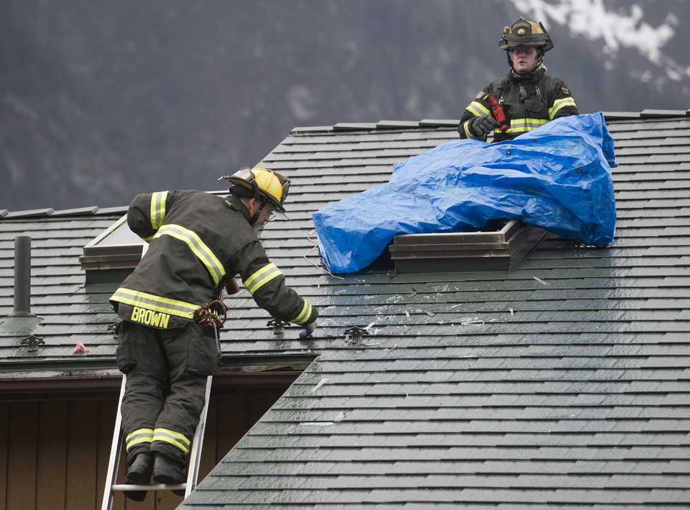 Capital City Fire/Rescue firefighters Craig Brown, left, and Travis Wolfe use a tarp to cover a broken skylight in the 3200 block of Foster Avenue in West Juneau on Monday. CCFR had to break the skylight while fighting a fire that started in a bedroom closet. CCFR Fire Chief Richard Etheridge said, "The smoke was clear down to the floor and it was super hot in there, so for them to find the fire they had to vent the smoke out." The fire was contained to the one room, but the upper floor suffered heavy smoke damage, according to Etheridge. The homeowner was taken to Bartlett Regional Hospital for a minor injury to the top of his head while fighting the fire.