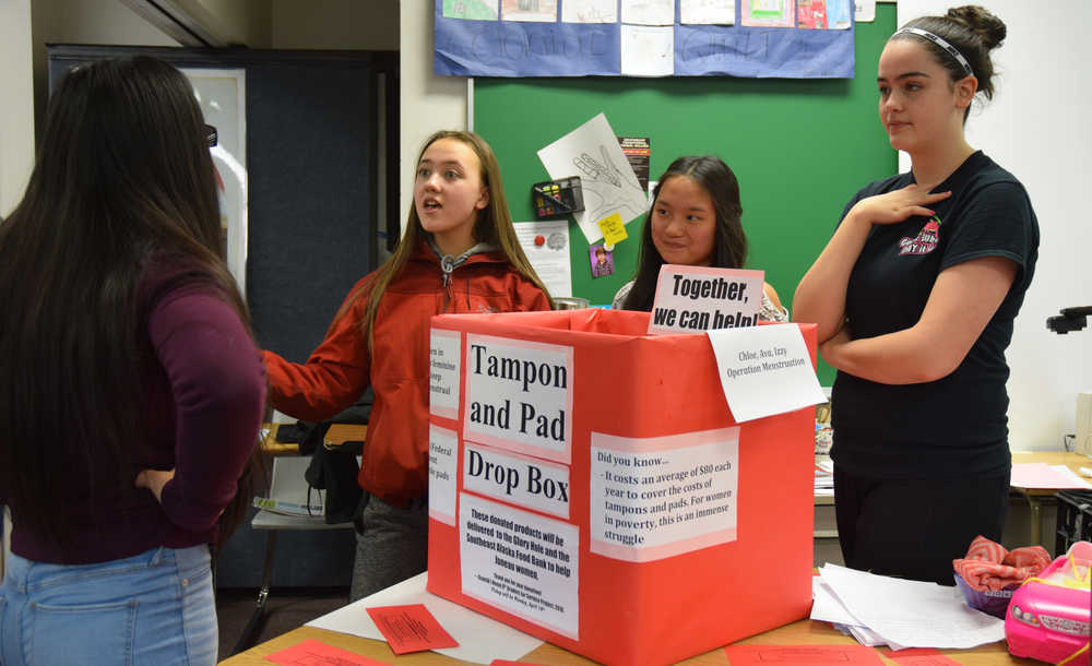Izzy Luna (far left) explains to a fellow eight-grader the struggles impoverished women face to meet feminine hygiene needs during a fair at Dzantik'i Heeni Middle School. Luna and her project partners - Ava Brown and Chloe McAdams (from left to right) took the issue on for a language arts class project. The girls are collecting tampons, panty liners and pads at school and at Safeway to give to Juneau women in need.
