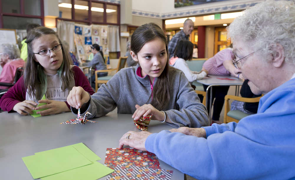 Harborview Elementary School fifth-graders Reece Hill, center, and Lauren Purves teach Pioneer Home resident Lenore Honsinger how to make paper cranes during a visit on Thursday.