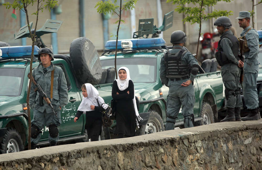 Afghan schoolgirls walk pass police forces near the site of a deadly Taliban-claimed suicide attack in Kabul, Afghanistan, Tuesday, April 19, 2016. Armed militants in Afghanistan have staged a coordinated assault on a key government security agency in the capital Tuesday morning, killing many and wounding more than 320 people. (AP Photo/Massoud Hossaini)