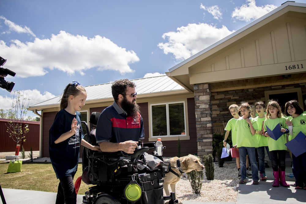 Thomas McRae, his 8-year-old daughter Aidan and his service dog Vera enter their new "smart home" in Maple Hill, North Carolina. Second-grade students at Jacksonville Montessori School, where Aidan goes to school, sing during the Stephen Siller Tunnel to Towers Foundation dedication ceremony on April 7.
