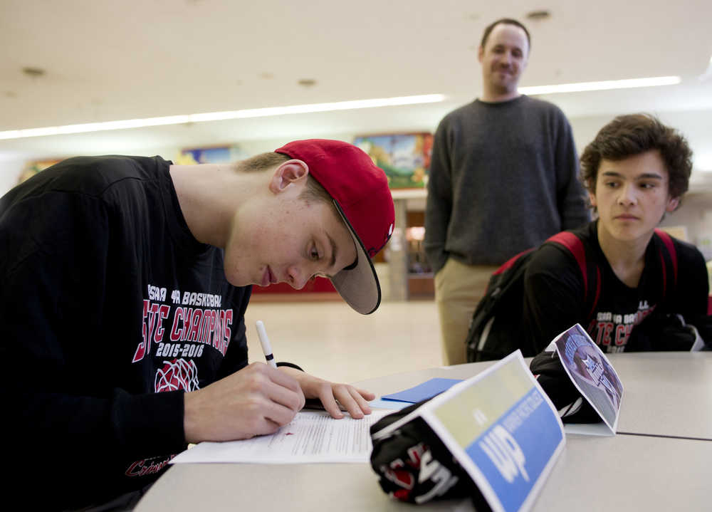 Kaleb Tompkins signs his letter of intent to Warner Pacific College as senior Treyson Ramos and basketball coach Robert Casperson watch at Juneau-Douglas High School on Thursday.